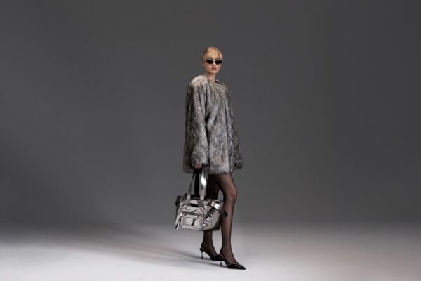 Stylizacje z answear.com: Kobieta w zimowym płaszczu z elegancką chustą w paski na głowie i okularami przeciwsłonecznymi podczas opadów śniegu. Stylizacja uzupełniona klasyczną torebką Saint Laurent z czarną skórą pikowaną i złotym logo YSL. Modny look na ulicach miasta w zimowym klimacie.