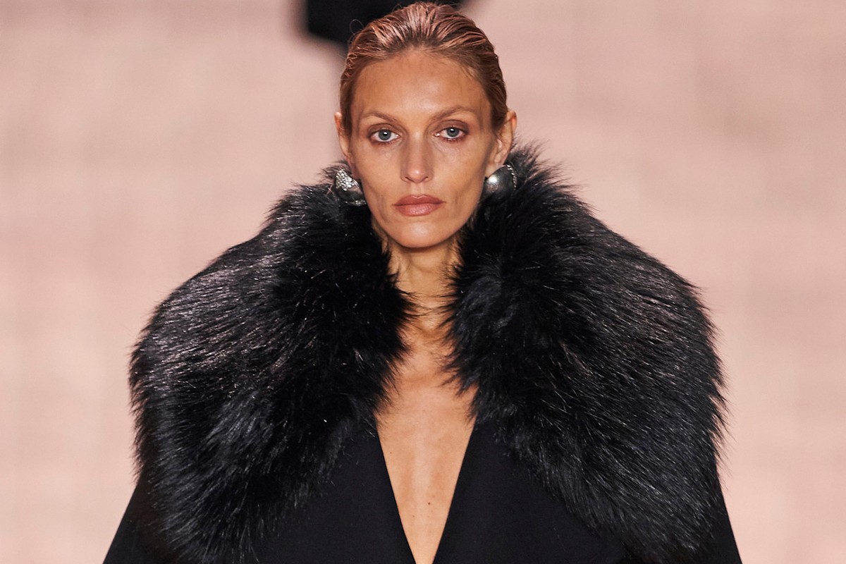 Anja Rubik na wybiegu Saint Laurent podczas prezentacji kolekcji na sezon jesień-zima 2022. Modelka jest w czarnym płaszczu z futrzanym kołnierzem, a na uszach ma srebrne kolczyki.
