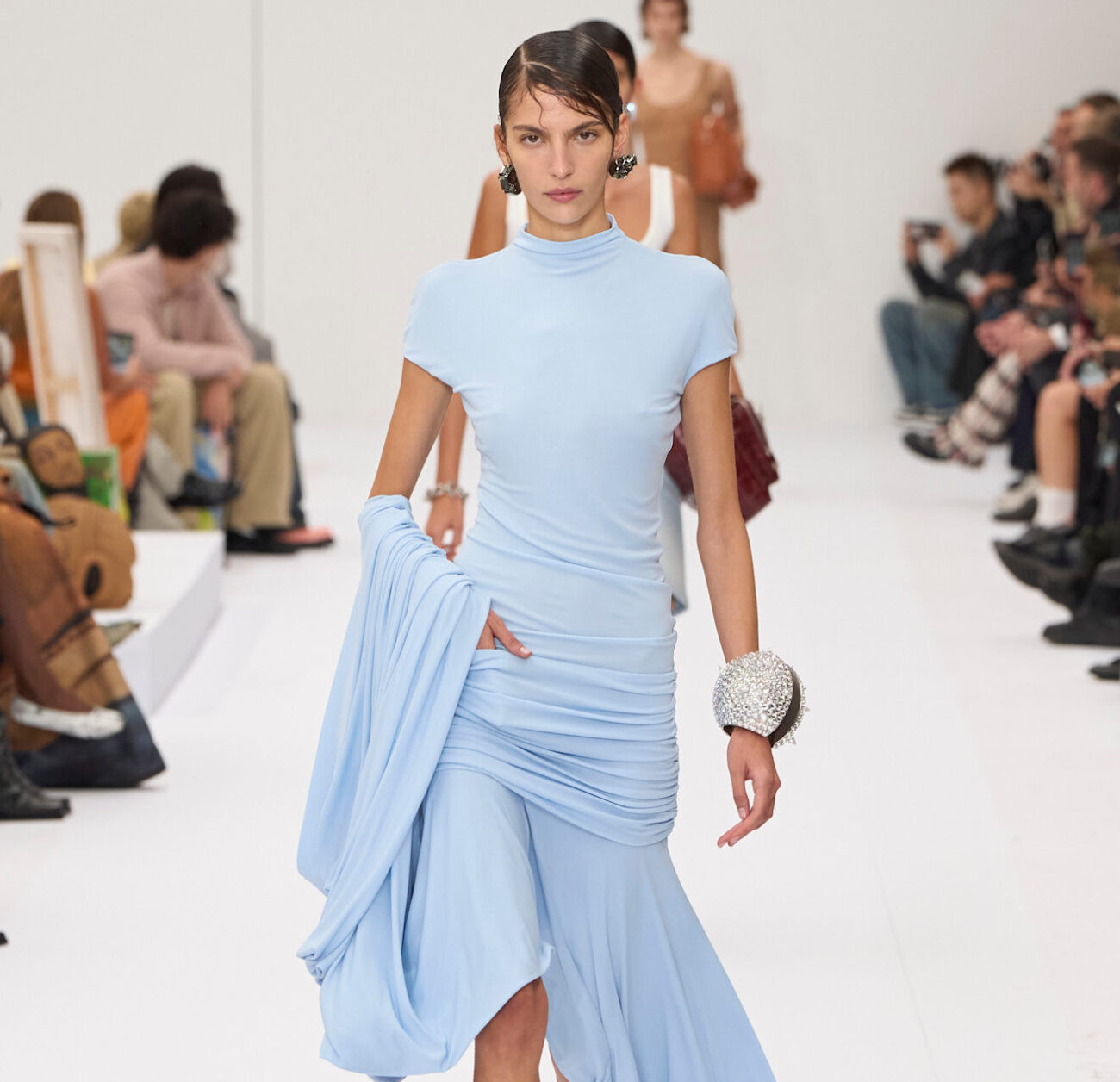 Stylizacja autorstwa Acne Studios – jasnoniebieska suknia z wysokim kołnierzem, drapowaniem w talii i asymetrycznym dołem. Całość dopełnia srebrzysta biżuteria i czarne buty na obcasie.