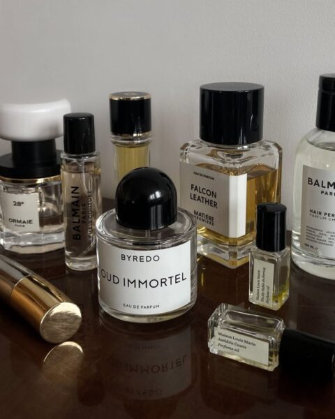 Zdjęcie przedstawia szafkę z ciemnym, drewnianym blatem, na którym stoją flakony z perfumami.