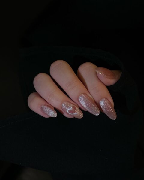 Modne paznokcie na luty 2025: Subtelny manicure w naturalnym odcieniu beżu z efektem magnetycznym tworzącym delikatne serca. Paznokcie są długie i migdałowe, a tło ciemne, co podkreśla ich elegancję.
