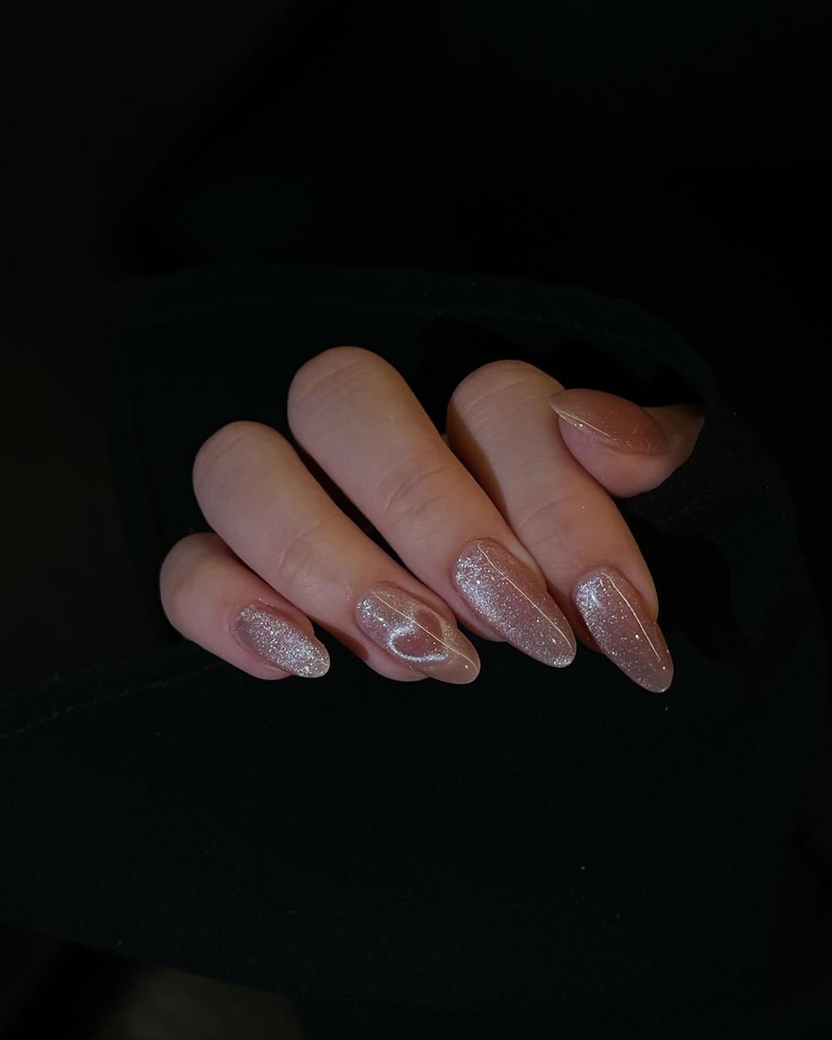 Modne paznokcie na luty 2025: Subtelny manicure w naturalnym odcieniu beżu z efektem magnetycznym tworzącym delikatne serca. Paznokcie są długie i migdałowe, a tło ciemne, co podkreśla ich elegancję.