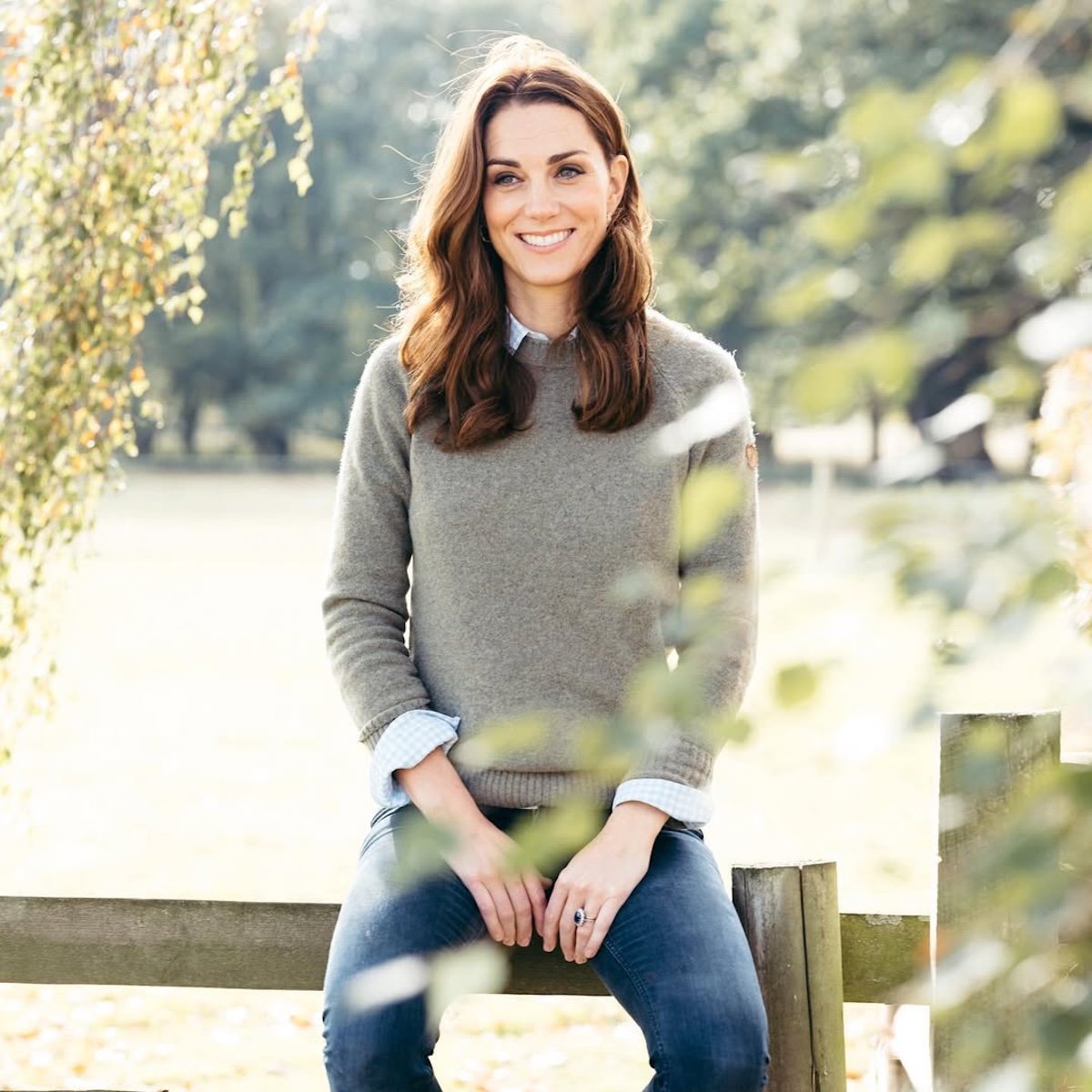 Kate Middleton choroba: Kobieta w casualowym stroju, siedząca na drewnianym płocie, otoczona zielenią.