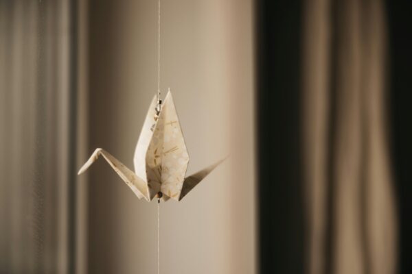 Kultura Japonii dla Dzieci: Zdjęcie przedstawia zawieszoną na nitce papierową figurkę origami żurawia, wykonane z wzorzystego papieru w ciepłym świetle.