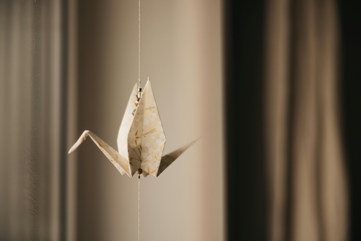 Kultura Japonii dla Dzieci: Zdjęcie przedstawia zawieszoną na nitce papierową figurkę origami żurawia, wykonane z wzorzystego papieru w ciepłym świetle.