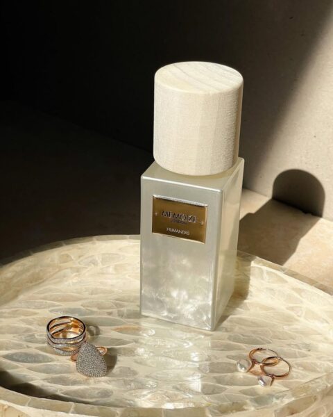 Perfumy z feromonami w kremowym flakonie z perłowym wykończeniem i drewnianą zatyczką. Perfumy znajdują się na perłowej tacce, a wokół leżą pierścionki i kolczyki.