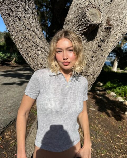 Gigi Hadid pozująca w promieniach słońca prezentując modną fryzurę na wiosnę 2025. Krótkie, rozjaśnione pasma pasują do jej twarzy, rozświetlając ją.
