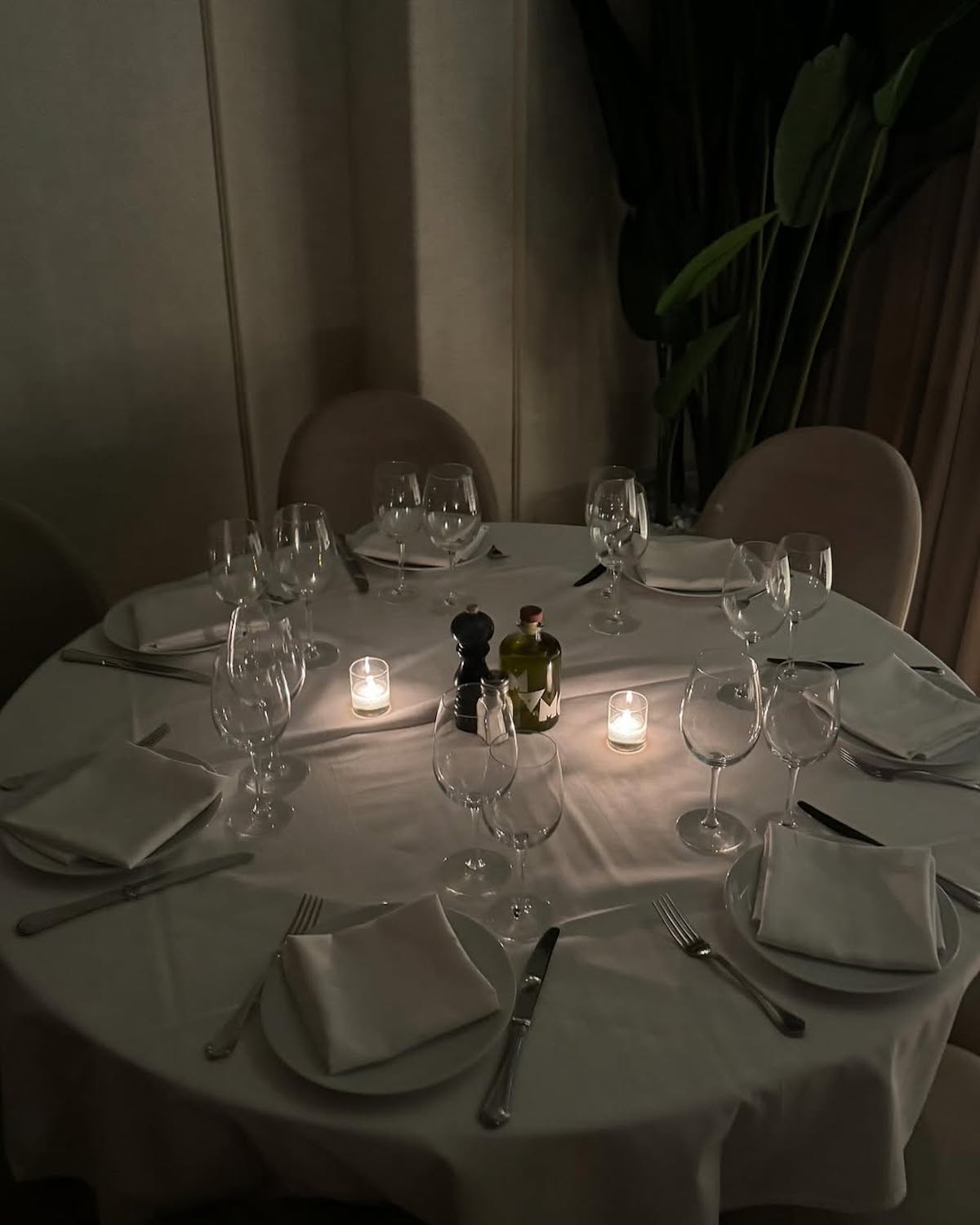 Elegancko nakryty stół w restauracji z białym obrusem, kieliszkami do wina, złożonymi serwetkami i świecami tworzącymi intymną atmosferę. W tle duża roślina dodająca naturalnego akcentu. Zdjęcie ukazuje wyrafinowany klimat miejsc z kategorii najlepsze wegańskie restauracje w Warszawie 2025.