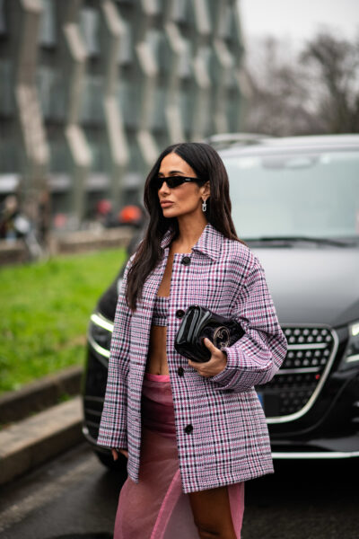 Fiolet na wiosnę 2025: Kobieta w różowym komplecie w pepitkę i przezroczystej spódnicy – modna stylizacja w stylu glamour ze skórzaną torebką Gucci, czarnymi okularami przeciwsłonecznymi i dopasowanym topem. Całość balansuje między klasyką a seksowną nonszalancją, idealnie wpasowując się w miejską modę uliczną.