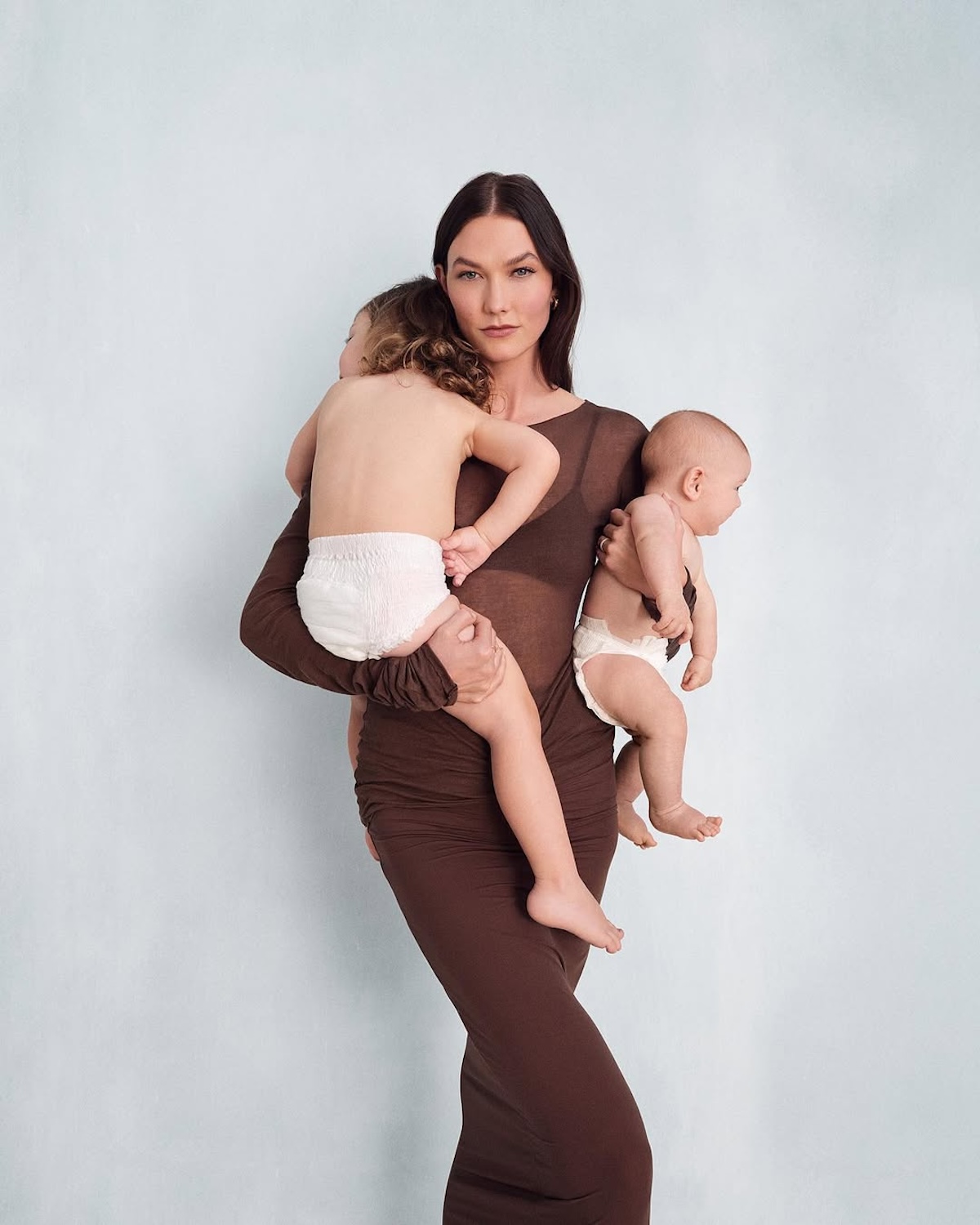 Karlie Kloss w ciąży: Modelka pozująca ze swoją dwójką dzieci w pampersach, ubrana w prześwitującą brązową sukienkę.