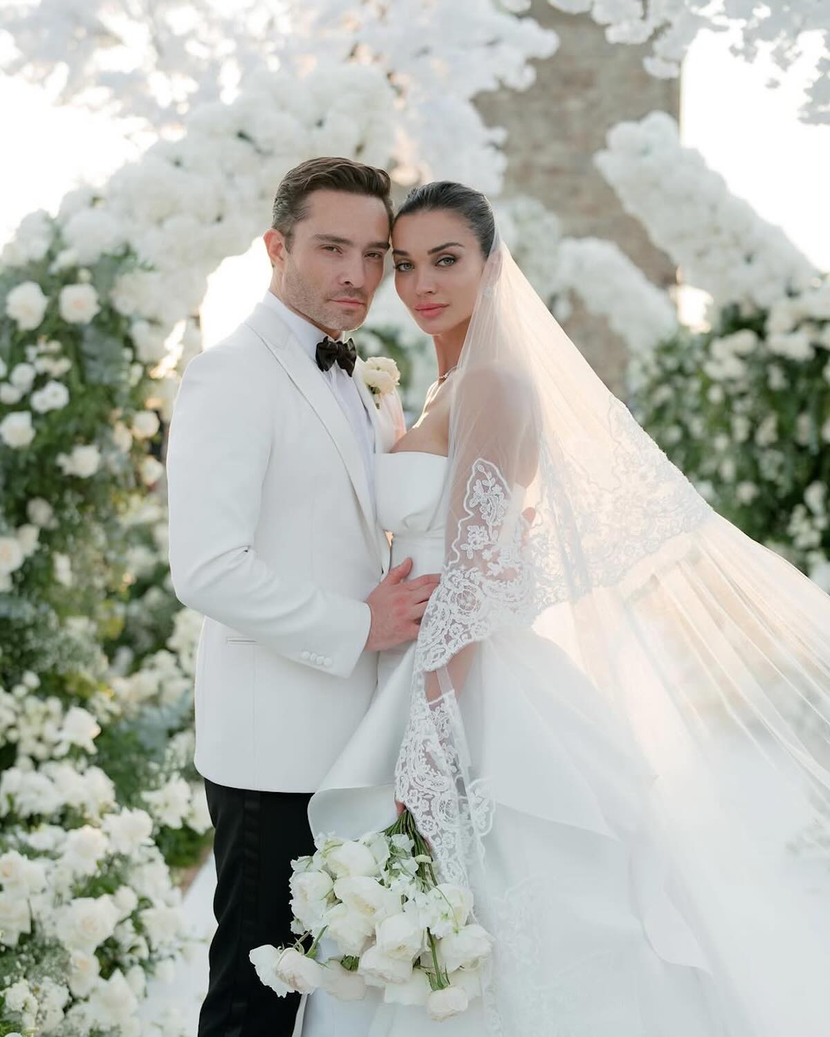 Ed Westwick, znany z roli Chucka Bassa w „Gossip Girl”, i jego żona Amy Jackson pozują do romantycznego zdjęcia ślubnego w bajkowej scenerii kwitnących białych kwiatów. Ona w koronkowym welonie i sukni z trenem, on w białej marynarce i muszce. Styl, elegancja i emocje zapowiadają nowy rozdział w ich wspólnym życiu jako małżonkowie i rodzice Oscara Alexandra Westwicka.
