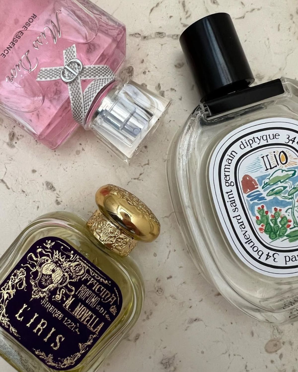 Zdjęcie przedstawiające zapachy vintage ułożone na kamiennym blacie. Widać perfumy w kolorze różowym, złote oraz przezroczyste.