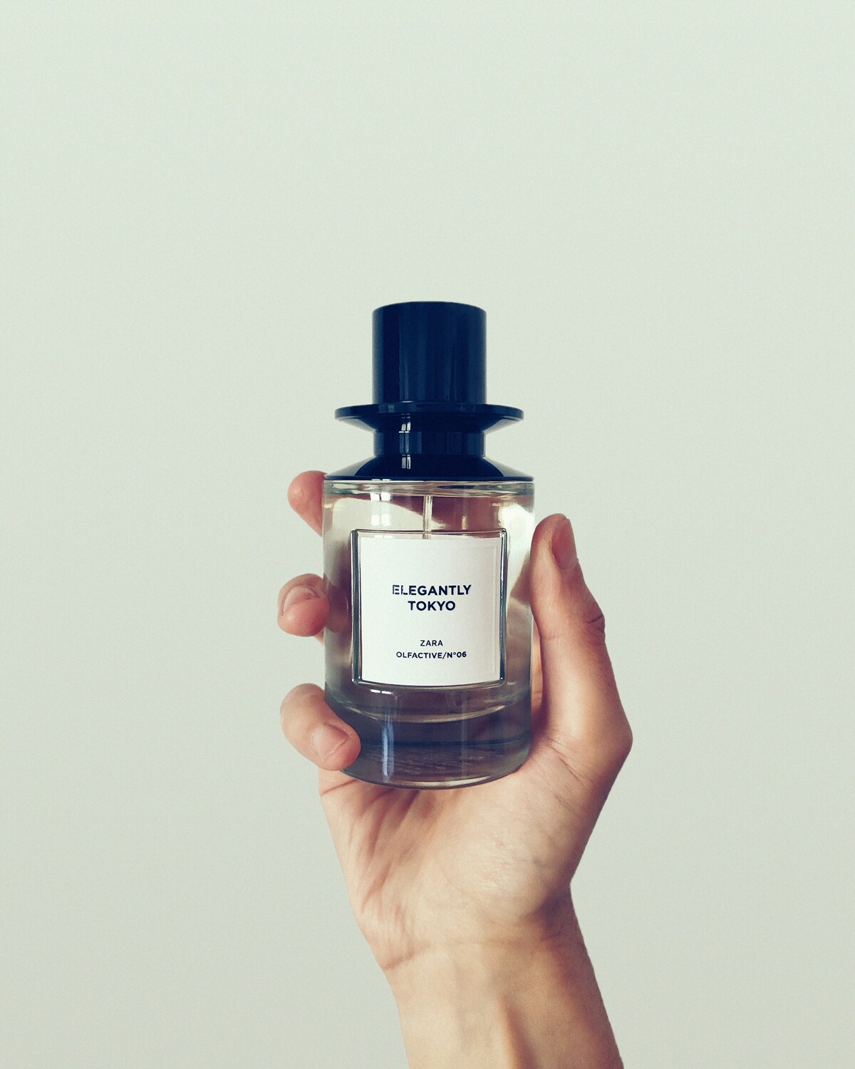 Perfumy z Zary zamienniki. Zdjęcie przedstawia rękę trzymającą perfumy z Zary Elegantly Tokyo, w szklanym minimalistycznym flakonie z czarnym zamknięciem.