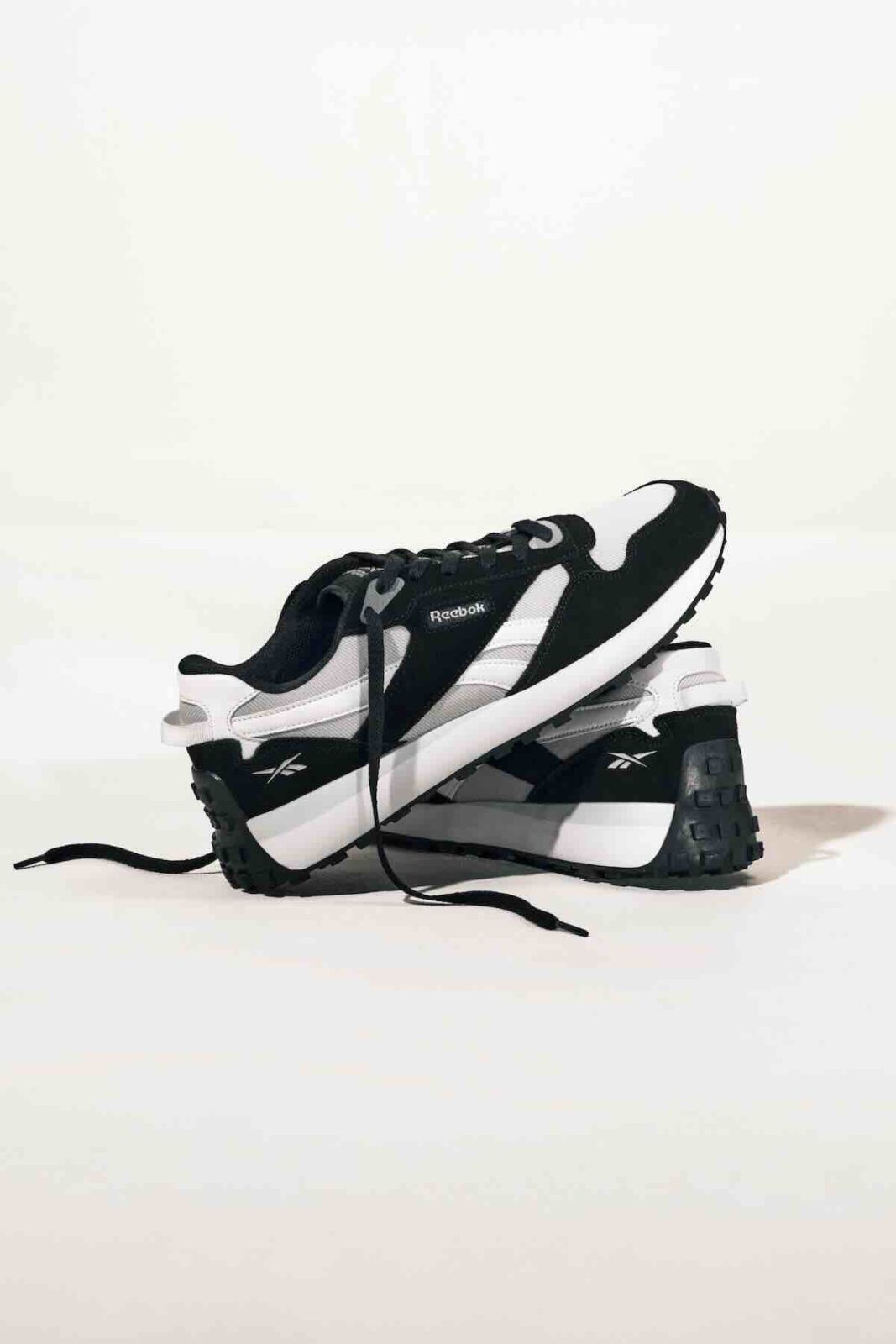 Para retro sneakersów Reebok w klasycznym połączeniu czerni i bieli, z charakterystycznym logo i grubą podeszwą – połączenie miejskiego luzu i oldschoolowej estetyki.