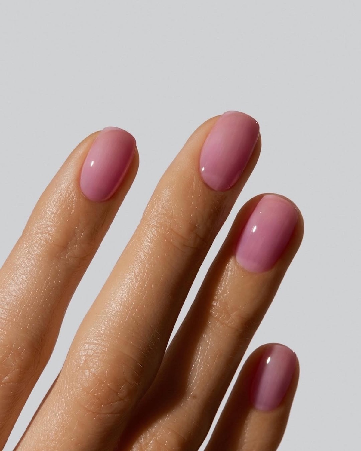 Jelly nails 2025. Zbliżenie na damską dłoń z jasnoróżowymi krótkimi paznokciami z efektem galaretki.
