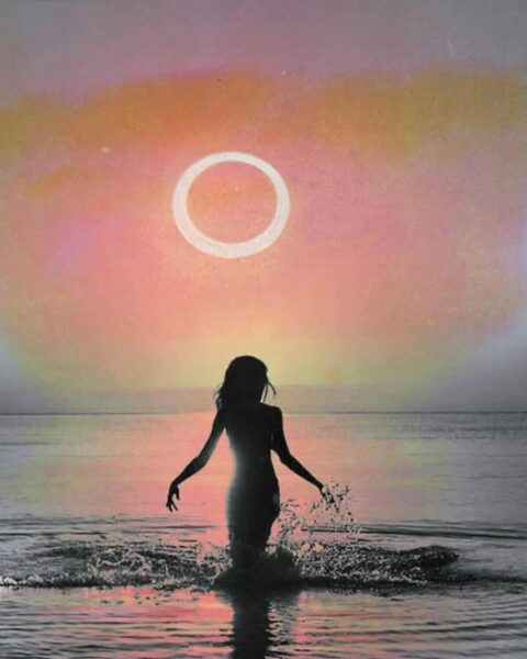 Ilustracja przedstawiająca sylwetkę osoby stojącej w wodzie podczas zachodu słońca, w kontekście koniunkcji dolnej Wenus w 2025. Na niebie widoczny jest jasny pierścień przypominający zaćmienie słońca lub inny fenomen astronomiczny. Niebo ma różowo-pomarańczową barwę, a woda odbija te kolory. Osoba stoi w wodzie, tworząc wokół siebie rozpryski.