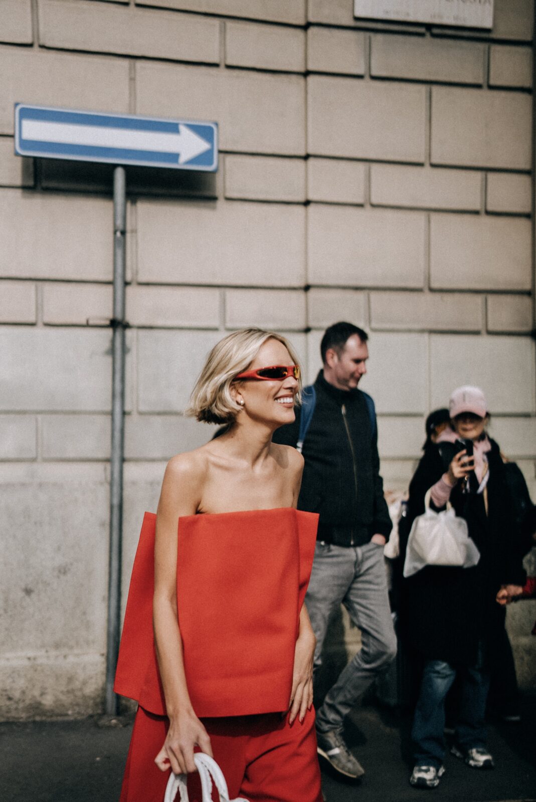 Trendy street style z Mediolanu: Odważna stylizacja w czerwieni – Kobieta w minimalistycznym, geometrycznym topie bez ramiączek i szerokich czerwonych spodniach. Jej futurystyczne okulary przeciwsłoneczne dodają całej stylizacji awangardowego charakteru.