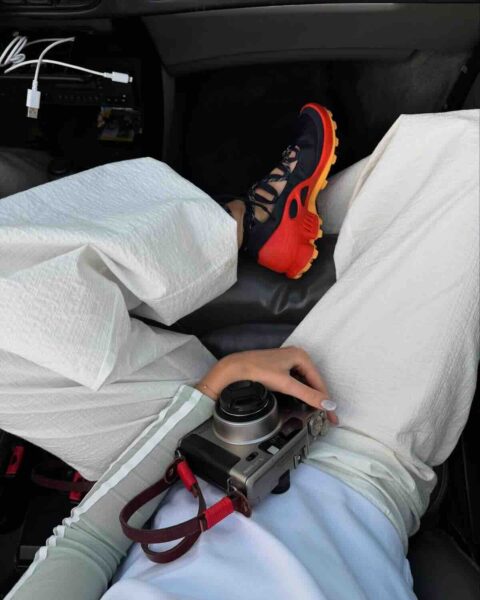 Zakaz fotografowania ustawa: Kobieta ubrana na biało i z kolorowymi sneakersami trzyma aparat na kolanach.