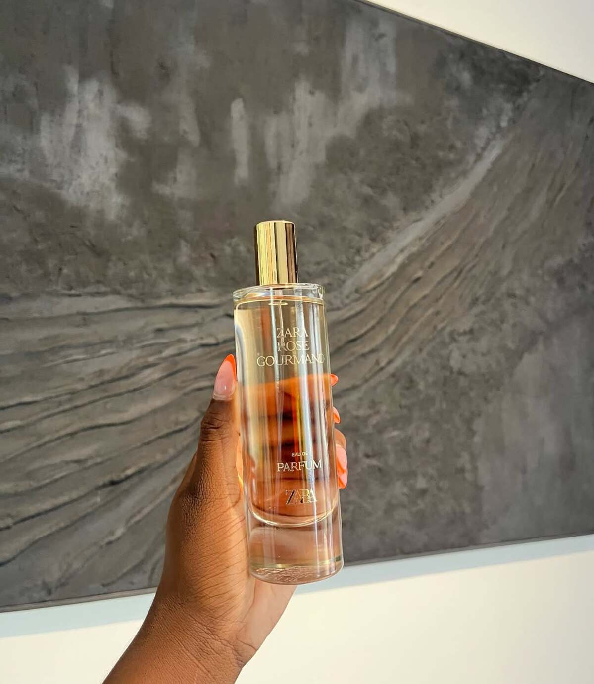 Perfumy z Zary na lato 2025 ranking. Kobieca dłoń trzymająca flakonik z perfumami z Zary ze złotym atomizerem. Buteleczka jest pełna, widać na niej złoty napis "Zara Rose Gourmand".
