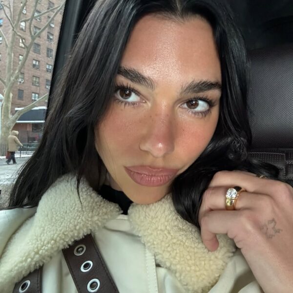 Jak dobrać kształt brwi do twarzy? Dua Lipa z gęstymi, naturalnymi brwiami pozuje w jasnej kurtce z kołnierzem z kożuchem.