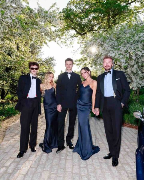 Brooklyn Beckham konflikt: Rodzina Beckhamów w wieczorowych kreacjach pozująca w ogrodzie – Grupa pięciu osób ubrana w czarno-granatowe smokingi i jedwabne suknie pozuje na tle kwitnącego ogrodu i brukowanego dziedzińca, promieniejąc elegancją i zgraniem stylizacji.