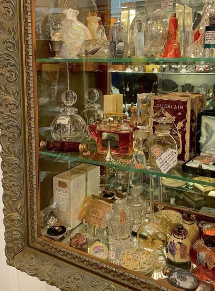 Stara przeszklona witryna z kolekcją historycznych flakonów perfum, w tym Guerlain, Escada, Joy Jean Patou i wiele innych. Luksusowe opakowania, zdobienia retro i ręcznie pisane etykiety tworzą atmosferę zapachowej nostalgii i olfaktorycznej podróży w czasie.