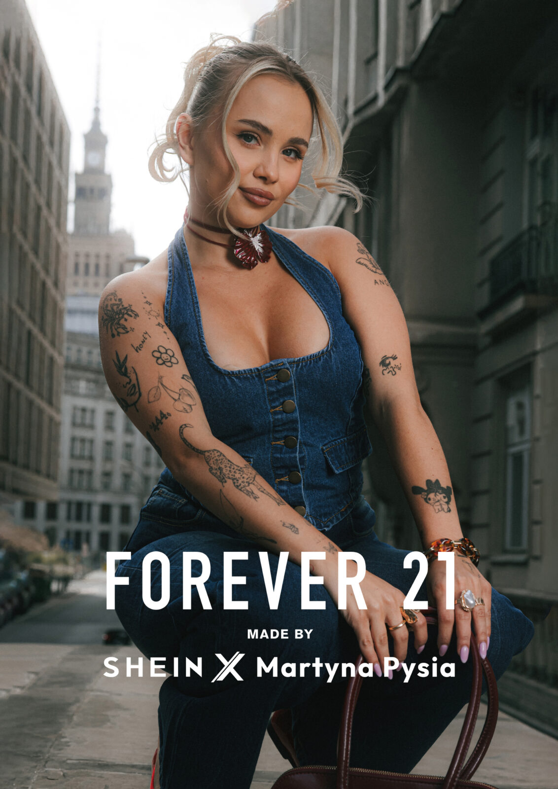Stylizacje Martyny Zabierajskiej: Martyna Pysia w kampanijnym ujęciu promującym kolekcję Forever 21 x SHEIN. Ubrana w dżinsowy top na ramiączkach, pozuje na tle Pałacu Kultury i Nauki. U dołu widoczne logo Forever 21 oraz napis „MADE BY SHEIN x Martyna Pysia”. Zdjęcie symbolizuje połączenie światowej marki z osobistym stylem influencerki.