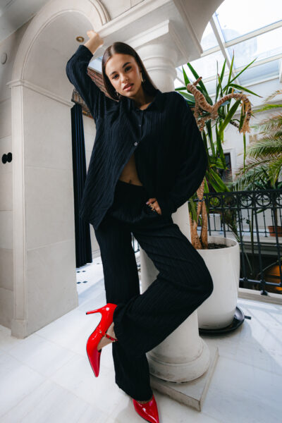 Stylizacje Anastasii Zakhandrevych: Look total black z czerwonym akcentem – Anastasiia w czarnym komplecie z plisowanej tkaniny i lakierowanych szpilkach. Stylizacja łączy miejski szyk z nonszalancką elegancją, zgodnie z estetyką Rafferiza.