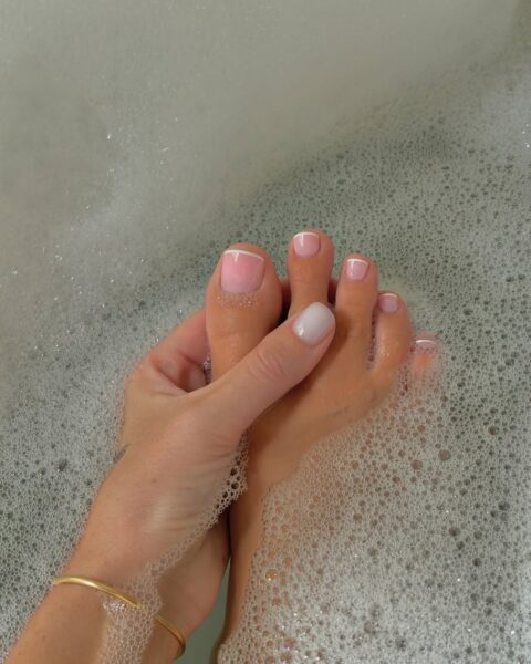 Pedicure french na lato 2025: Stopy z francuskim pedicure zanurzone w kąpieli z pianą. Subtelny kontrast mlecznoróżowej bazy i klasycznego białego paska tworzy zmysłowy efekt w domowym rytuale pielęgnacyjnym.