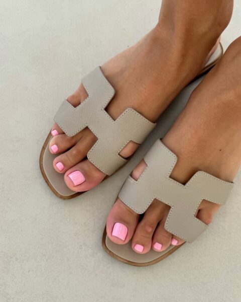 Liliowy pedicure na pięknie opalonych stopach w klapkach Hermes.