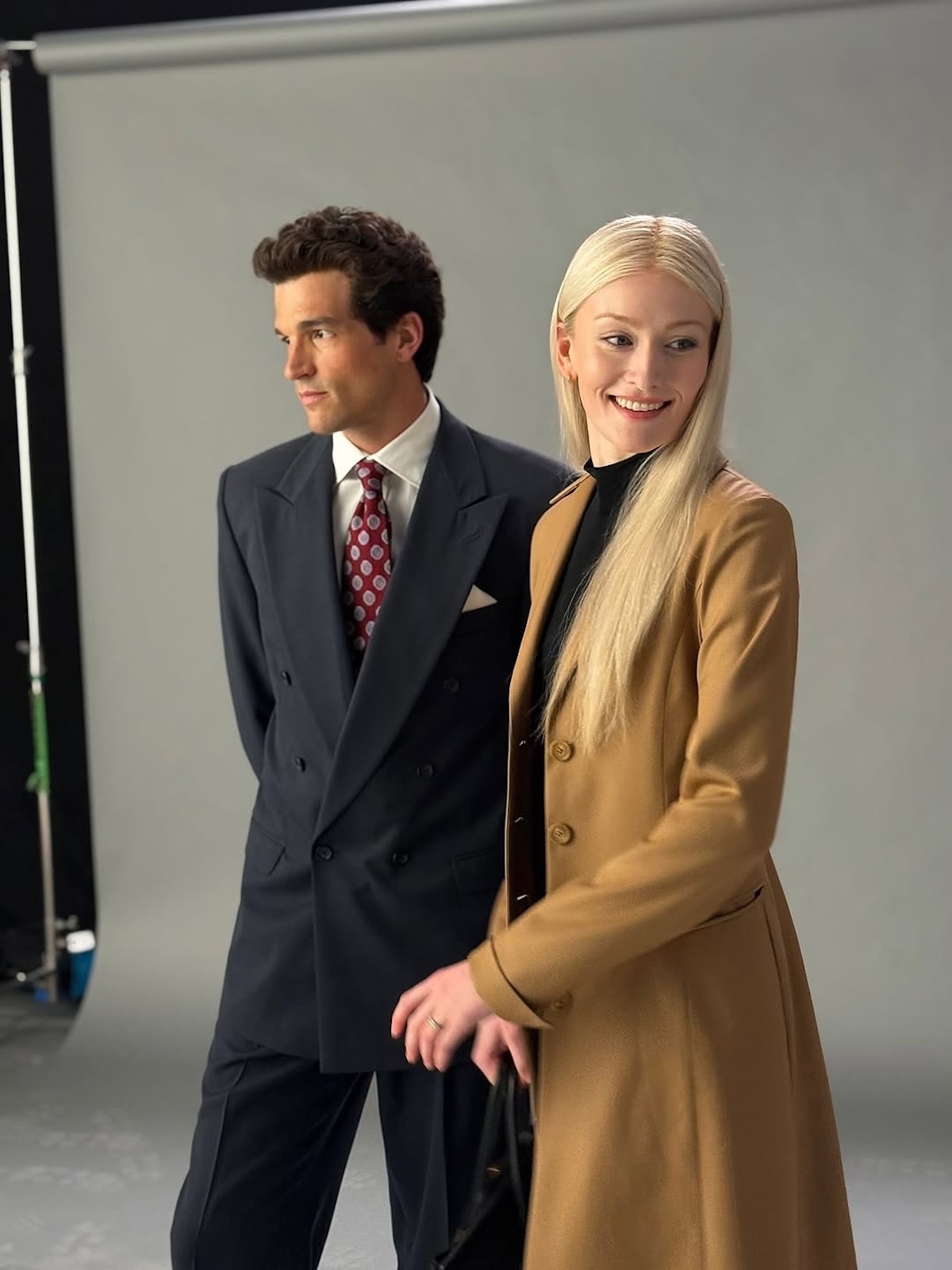American Love Story: Sarah Pidgeon w roli Carolyn Bessette w minimalistycznym looku z charakterystycznym camelowym płaszczem, czarnym golfem i spodniami cygaretkami; całość dopełnia klasyczna torebka Birkin – odtworzenie ponadczasowej estetyki „quiet luxury”.