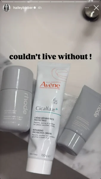 Zdjęcie kosmetyków do pielęgnacji skóry na marmurowym blacie, udostępnione na Instagram Stories przez haileybieber. Widać trzy produkty: Rhode Glazing Milk (szare opakowanie), Avène Cicalfate+ Repairing Protective Cream (biała tubka) i Rhode Barrier Butter (mniejsze szare opakowanie). Na górze napis 'couldn’t live without!'.