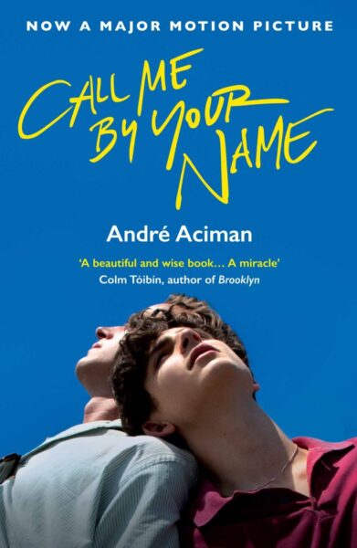 Okładka książki ‘Call Me by Your Name’ autorstwa André Acimana, z niebieskim tłem, żółtym tytułem zapisanym odręczną czcionką i zdjęciem dwóch młodych mężczyzn patrzących w górę, stojących blisko siebie. Na górze widnieje napis: ‘Now a major motion picture