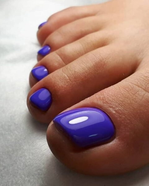 Zdjęcie stóp z granatowym pedicure w odcieniu borówki z lśniącym efektem glazed.