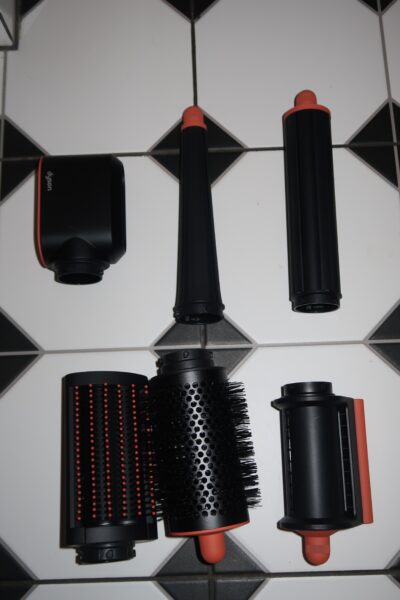 Multistyler Dyson Airwrap i.d.™ Straight+Wavy: Zamknięte etui Dyson Airwrap i.d.™ w intensywnym kolorze chabrowym, leżące na podłodze w stylu retro. Minimalistyczny design z delikatnym logo Dyson na wieczku. Opakowanie premium pasujące do nowoczesnej łazienki.