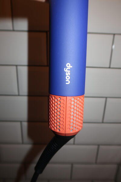 Zbliżenie na górną część zamkniętego etui Dyson Airwrap i.d.™ Straight+Wavy w kolorze chabrowym. Wyraźnie widoczne tłoczone logo „Dyson” na matowej powierzchni. Stylowy detal wykończeniowy.