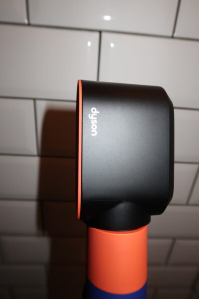Dolna część korpusu multistylera Dyson Airwrap i.d.™ Straight+Wavy w odcieniach pomarańczowym i niebieskim. Zbliżenie na kratkę wentylacyjną i kabel zasilający. Elementy pokazujące dbałość o detale i jakość wykonania.