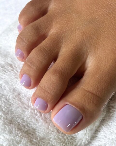 Zdjęcie stóp ze zbliżeniem na lawendowy pedicure. Stopy są tuż po stylizacji, pozują na białym ręczniku.