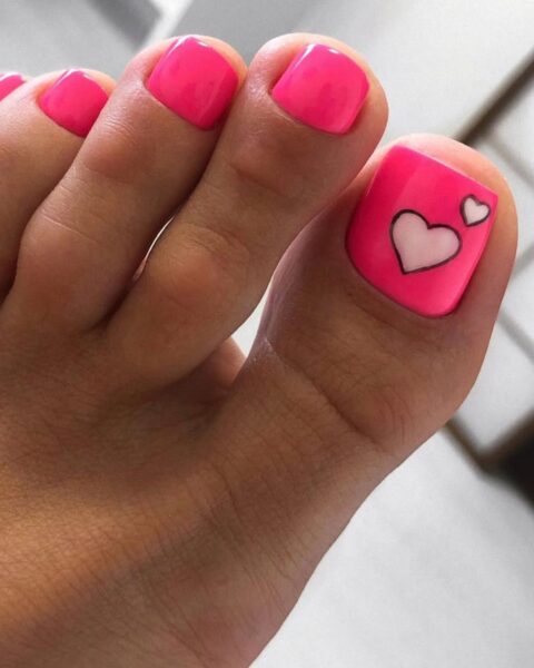 Zdjęcie stopy ze zbliżeniem na pedicure w kolorze różowym z ozdobnym wzorem serduszka na dużym palcu.