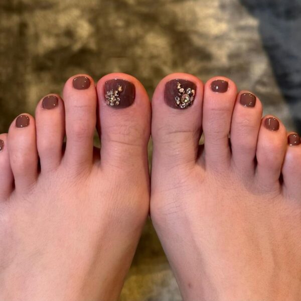 Podwójne stóp Jennifer Lopez ze zbliżeniem na jej pedicure: brązowy z kryształkami Svarovskiego na dużych palcach.