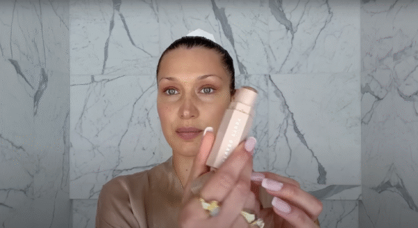 Bella Hadid prezentuje sztyft do konturowania Fenty Beauty Match Stix Matte Skinstick w łazience wyłożonej marmurem. Modelka z naturalnym makijażem i spiętymi włosami pokazuje swój ulubiony kosmetyk do modelowania twarzy.