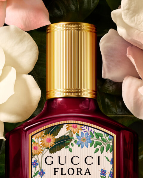 Artystyczne zbliżenie na górną część flakonu Gucci Flora Gorgeous Gardenia Intense, otoczonego płatkami kremowych i różowych kwiatów. Na zdjęciu wyeksponowano złotą zakrętkę oraz górny fragment dekoracyjnej etykiety z botanicznym motywem. Ujęcie podkreśla kunszt wykonania i poetyckość kompozycji wizualnej zapachu.