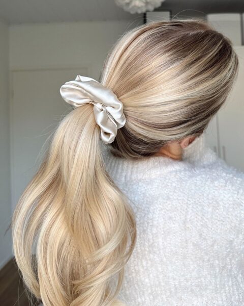 Zdjęcie kobiety stojącej tyłem. Ma blond włosy związane kremową scrunchie. Ubrana jest w kremowy sweter.