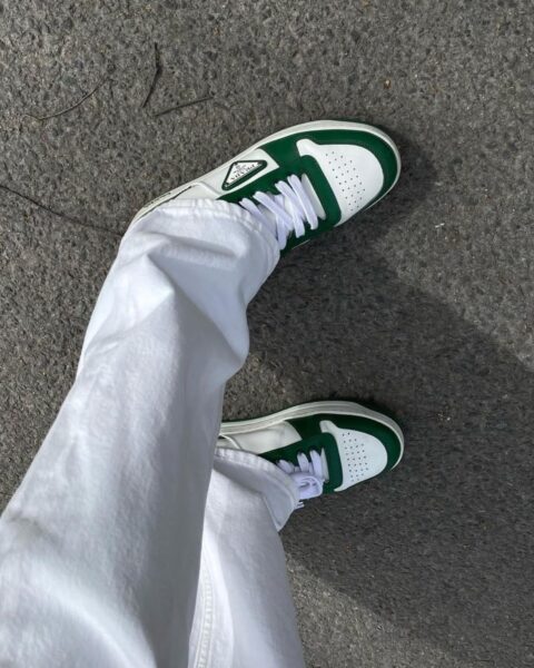 Zdjęcie nóg zrobione od góry na białe nogawki spodni i sneakersy Prada w kolorze biało-zielonym.