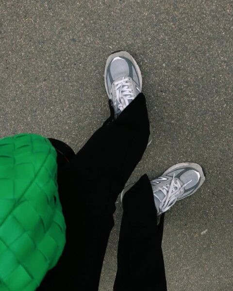 Zdjęcie nóg zrobione od góry: widać sneakersy New Balance, szerokie czarne spodnie i zieloną, plecioną torebkę Bottega Veneta.