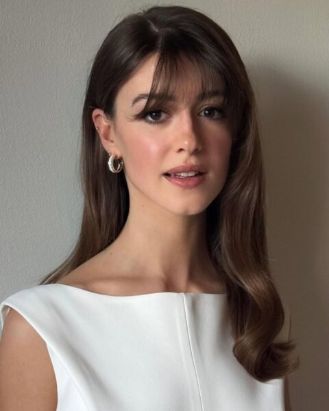 Zdjęcie aktorki Daisy Edgar Jones. Ma grzywkę typu thin bangs i długie włosy rozpuszczone na ramiona. Ubrana jest w biały top bez rękawów. W uszach kolczyki.