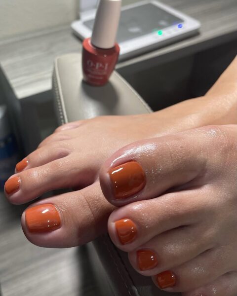 Pedicure na jesień 2025: paznokcie u stóp w ciepłym, ceglastym odcieniu pomarańczu, wykonane lakierem OPI. Stylizacja inspirowana jesienną paletą barw, przywodząca na myśl ceramikę i ciepło sezonowych przypraw.