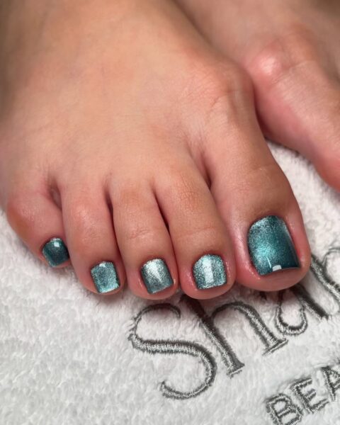 Zdjęcie stóp ze zbliżeniem na korean crystal cat eye pedicure w kolorze zielonym, czyli z kocim okiem w zieleni. Stopy pozują na tle ręcznika tuż po stylizacji.