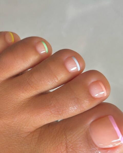 Zdjęcie stopy ze zbliżeniem na pedicure w stylu french z pastelowymi końcówkami. Na każdym paznokciu jest inny kolor.