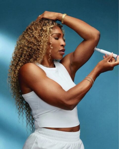 Na zdjęciu jest Serena Williams i Ozempic: kobieta wstrzykuje sobie preparat w ramię. Ubrana jest w biały top i białe szorty. Pozuje na niebieskim tle.